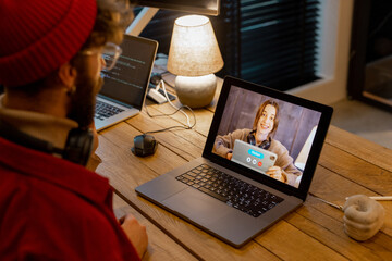 Stylish man in red hat having video call with female colleague while sitting at cozy home office. Concept of online meetings and remote work from home