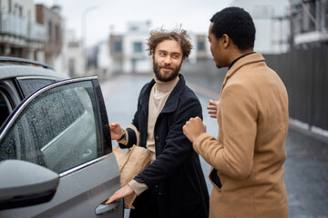 Two men flirting or having a close conversation while opening car door on the street. Concept of homosexual relations or close male friendship. Caucasian and hispanic man wearing coats