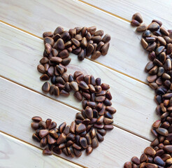 the figure five is laid out of large unpeeled pine nuts on a light wood background