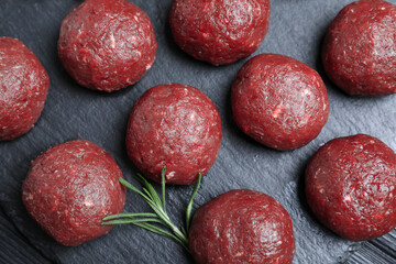 Many fresh raw meatballs with rosemary on black board, flat lay