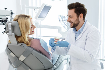 Obraz premium Cheerful man doctor dentist showing jaw miniature to patient