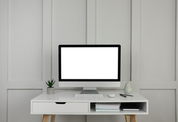 Modern computer, decor and office supplies on white wooden table near molding wall