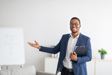 Friendly young African American psychologist with clipboard showing something with his hand at mental health clinic - obrazy, fototapety, plakaty