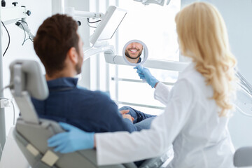 Female dentist holding mirror for smiling male patient