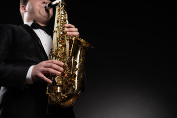 Fototapeta na wymiar Saxophonist Musician in Black Tuxedo and Bow Tie Plays the Alto Saxophone. Alto Sax Player, Jazz Sazophonist. Black Background. Close-up. Copy Space . High quality photo
