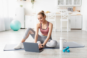 Smiling caucasian cute young blonde fitness blogger woman looking at laptop, chatting and choosing...