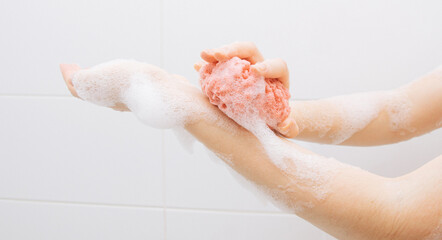 Fototapeta premium A girl in a white bathroom in foam rubs her hands with a pink washcloth