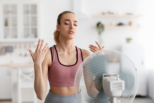 Tired Sad European Pretty Millennial Blonde Lady Stands In Front Of Fan Cooling Down After Workout At Home