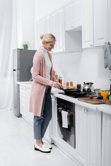 full length view of happy middle aged woman cooking pancake near fresh vegetables.