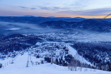 View from mount peak on Sheregesh ski resort and Altai mountains or Gornaya Shoria. Active winter rest, skiers and snowboarders on ski slope and Ski lift, nature and sport leisure.