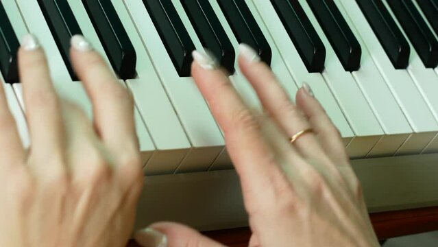 Close-up of female and children's hands playing the piano.Teaching a child to play a musical instrument. Music school online. Family leisure playing the piano.Selective focus