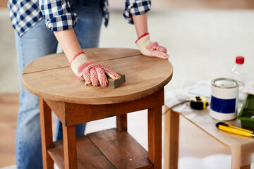 furniture renovation, diy and home improvement concept - close up of woman sanding old wooden table...