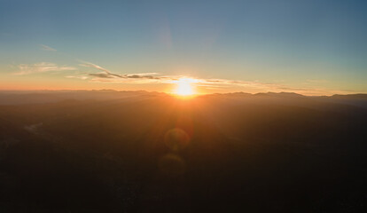 Aerial view of dark mountain hills with bright sunrays of setting sun at sunset. Hazy peaks and misty valleys in evening
