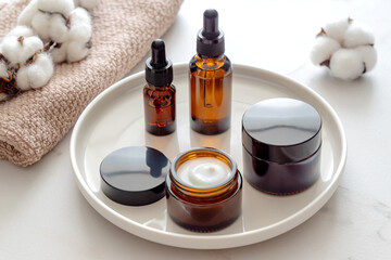 Set of amber glass cosmetic bottles on ceramic tray. dropper bottle and cream jar package. Skincare...