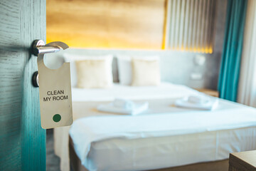 Opened door of hotel room. Door of hotel room with please make up room sign. Hotel room or apartment doorway with key and keyring key fob in open door and bedroom in background