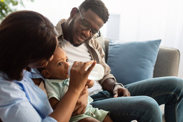 Happy African American parents feeding child from bottle