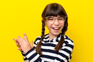 Little caucasian girl isolated on yellow background With glasses and applauding