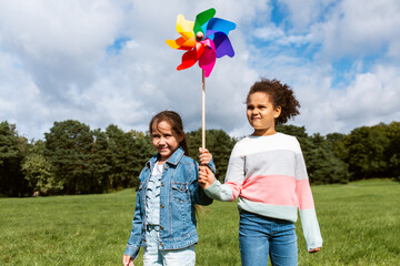 childhood, leisure and people concept - happy girls with pinwheel having fun at park