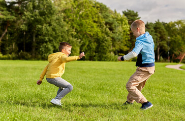 childhood, leisure and people concept - two happy boys playing tag game and running on lawn at park