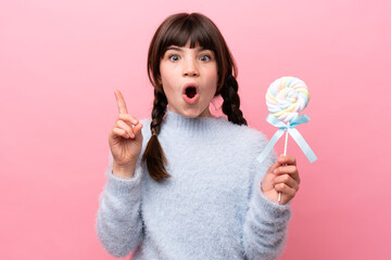Little caucasian girl holding a lollipop intending to realizes the solution while lifting a finger up