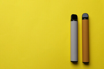 Different electronic cigarettes on yellow background, flat lay. Space for text