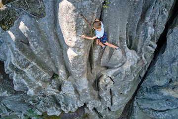 Young child boy climbing steep wall of rocky mountain. Kid climber overcomes challenging route....