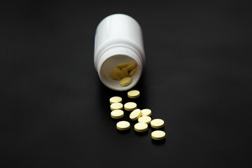 White plastic jar on a black background with poured pills.