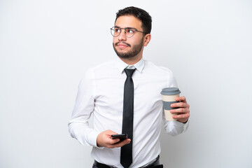 Business Brazilian man isolated on white background holding coffee to take away and a mobile while thinking something