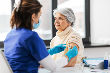 Obraz premium medicine, health and vaccination concept - doctor or nurse with syringe making vaccine or drug injection to senior woman at hospital