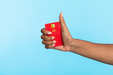 Cropped view of Afro woman holding red credit card and showing thumb up gesture on blue studio background