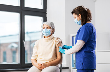 medicine, health and vaccination concept - doctor or nurse applying medical patch to vaccinated senior woman in mask at hospital