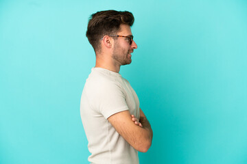 Young caucasian handsome man isolated on blue background in lateral position