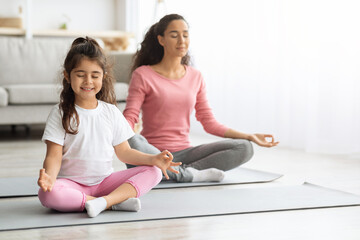 Cute little girl meditating with her mother at home