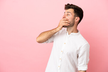 Young caucasian handsome man isolated on pink background doing surprise gesture while looking to the side