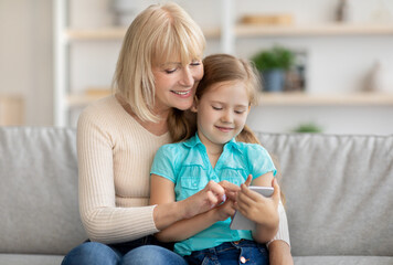 Happy mature woman and granddaughter using cellphone