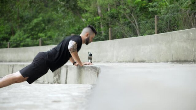 Athletic man doing push ups and triceps dip exercise in park. Fit guy in calisthenics training outdoors.
