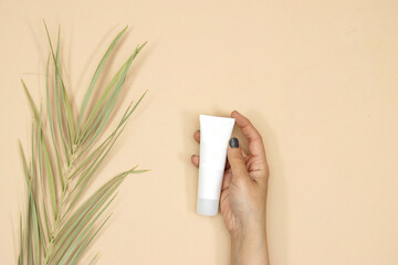 closeup hand woman holding Beauty cosmetics tube; branding mock up isolated on pink background. Package for hand cream or scrub. Beauty cosmetics tube, branding mock up with palm tree leaf 