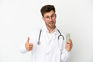 Young doctor caucasian man over isolated on white background wearing a doctor gown and holding pills
