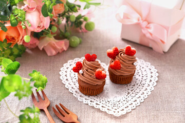 Chocolate cupcakes with chocolate cream with strawberry heart. 
Valentine bouquet of rose flowers  and gift.