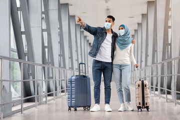Young Islamic Spouses Wearing Protective Medical Masks Standing With Suitcases In Airport
