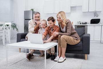 boy using laptop near smiling grandparents and sister in kitchen.