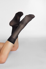 Cropped shot of slim woman's legs bent. The sexy girl is wearing black translucent knee socks with...