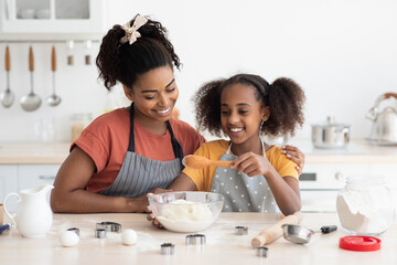 Black mother showing her teen daughter how to make cookies