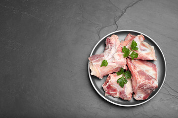 Plate with raw chopped meaty bones and parsley on black table, top view. Space for text