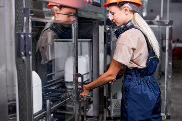 worker in factory preparing robotic line for bottling and packing canisters. Inspection of quality control. Professional engineer woman in blue uniform is getting ready to turn on the equipment