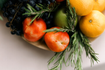 A fruit plate. Various fruits with rosemary on the table. Black grapes, nectarines, tangerines and green apples. 