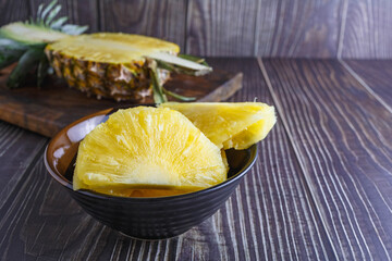Fresh pineapple halved with pineapple slices in bowl on wooden table