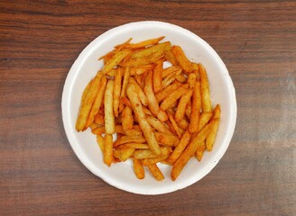 Traditional French fries or potato chips in white plate top view on dark wooden background