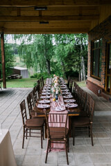 Fototapeta premium A beautiful outdoor wedding setting in pink flowers. plates and cutlery on a wooden table against a backdrop of greenery. On a Summer day a wooden reception table in the backyard, decorated with rose