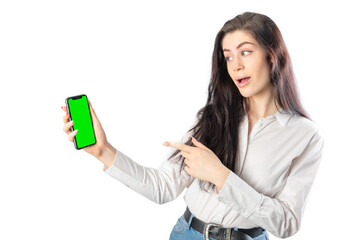 Amazed woman holding a smartphone (with green chroma key screen) looking it and pointing it with her finger. Isolated on white background. 20-22 years old. White european woman.